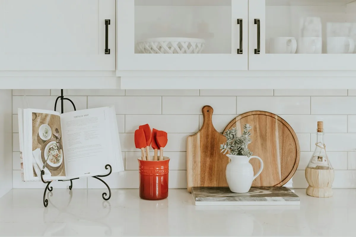 A white kitchen counter with wooden boards and cooking utensils