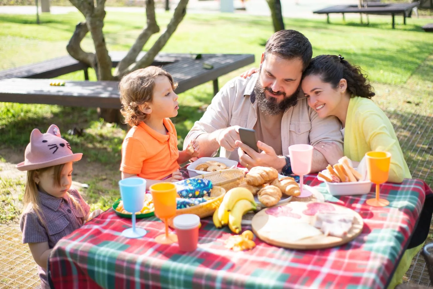 A family seated at an outdoor picnic table with breakfast food and drinks.