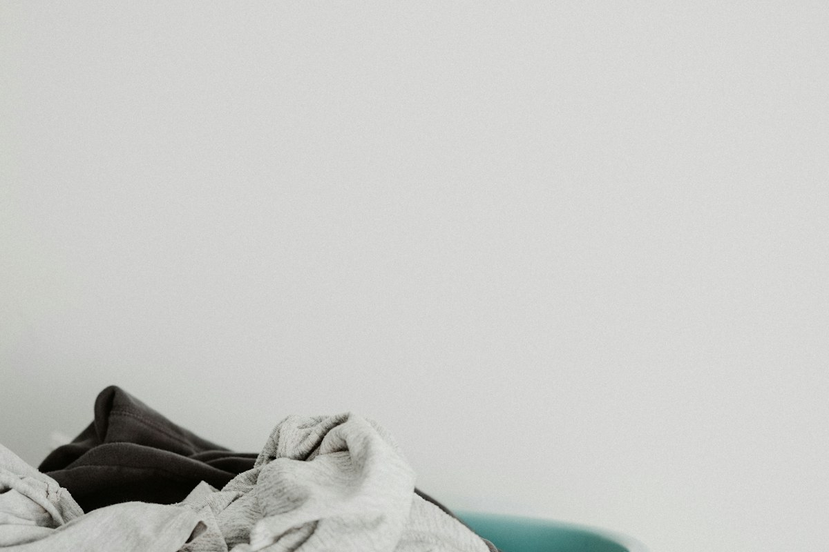 Light and dark textiles in a pale blue plastic laundry container.