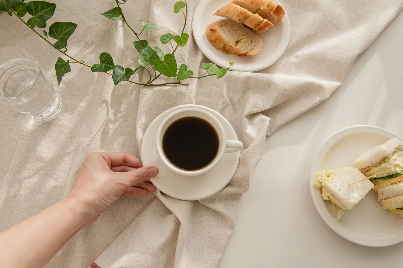 Coffee, sandwiches and bread arranged on a small table with a linen cloth.