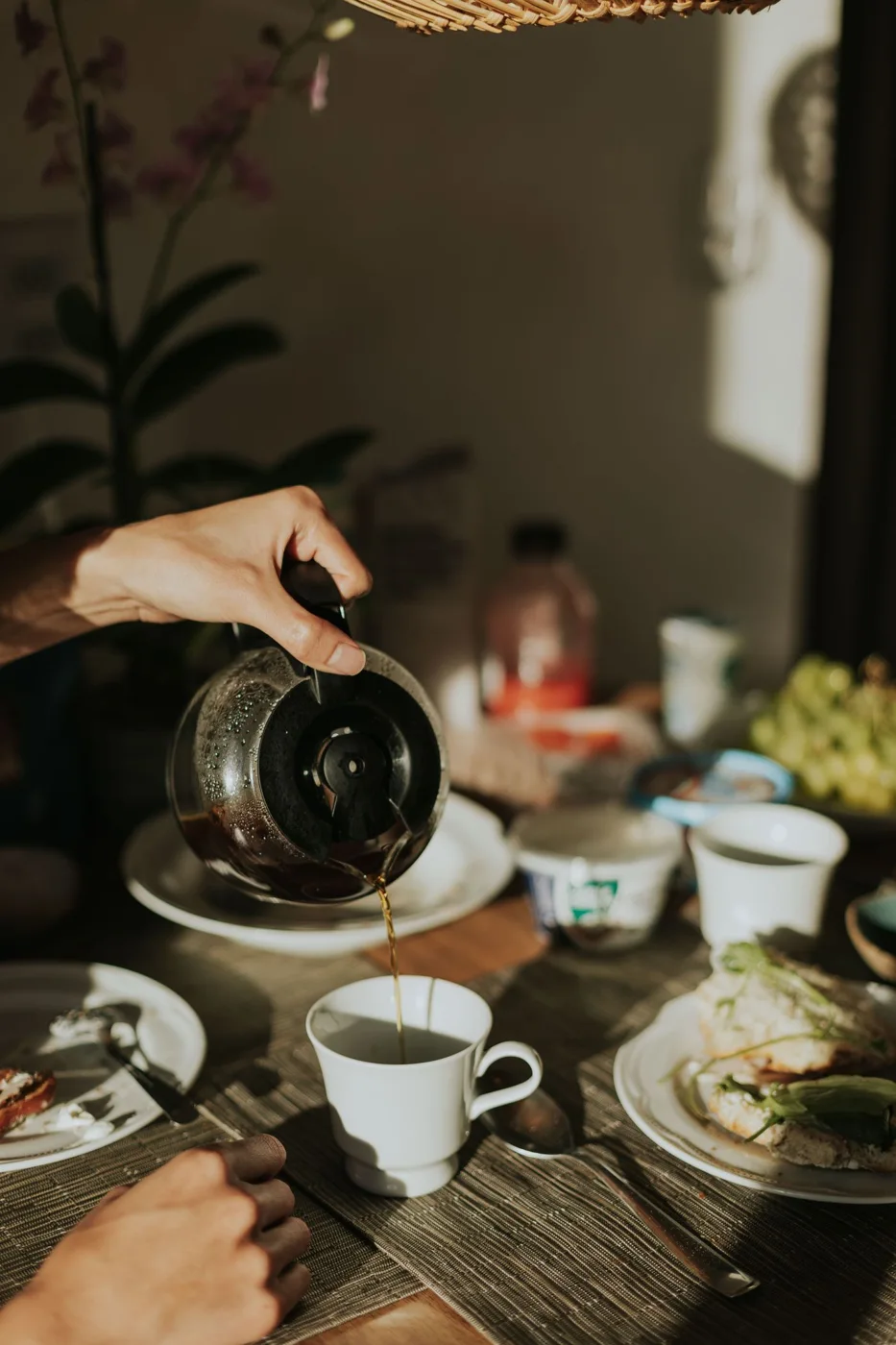 Coffee being poured from a glass pot beside breakfast tableware