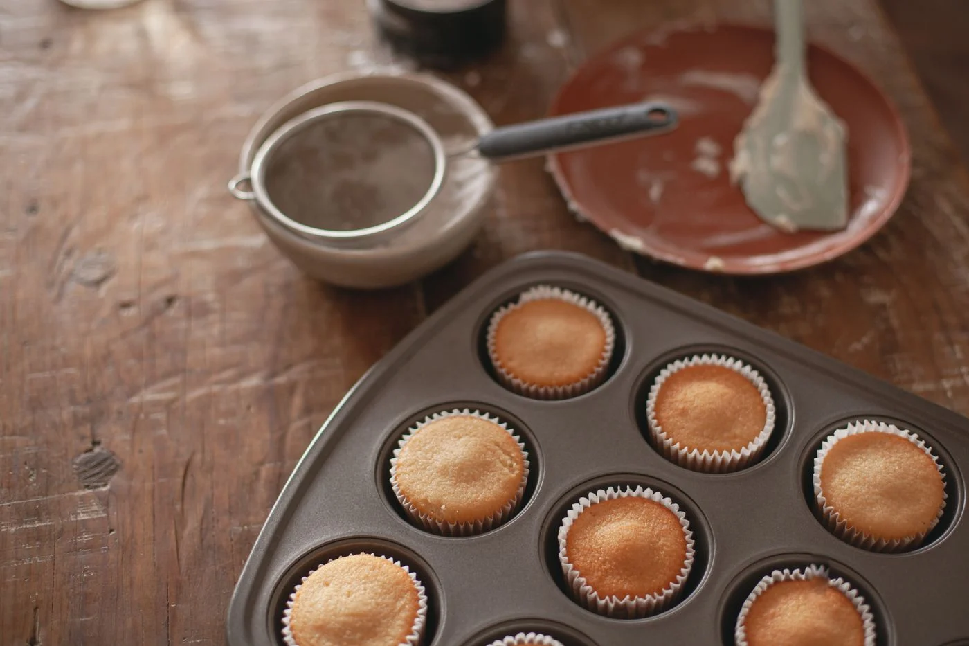 Baked cupcakes in a muffin tin beside baking equipment