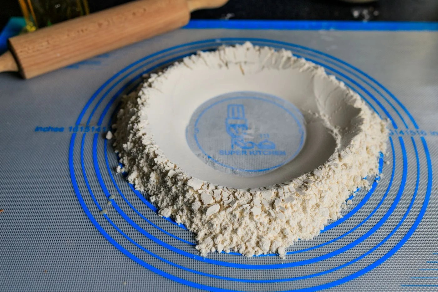 Flour arranged on a silicone mat beside a wooden rolling pin