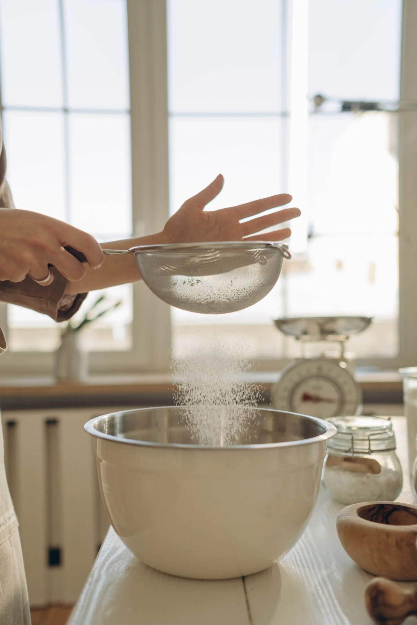 Hands sifting flour into a mixing bowl
