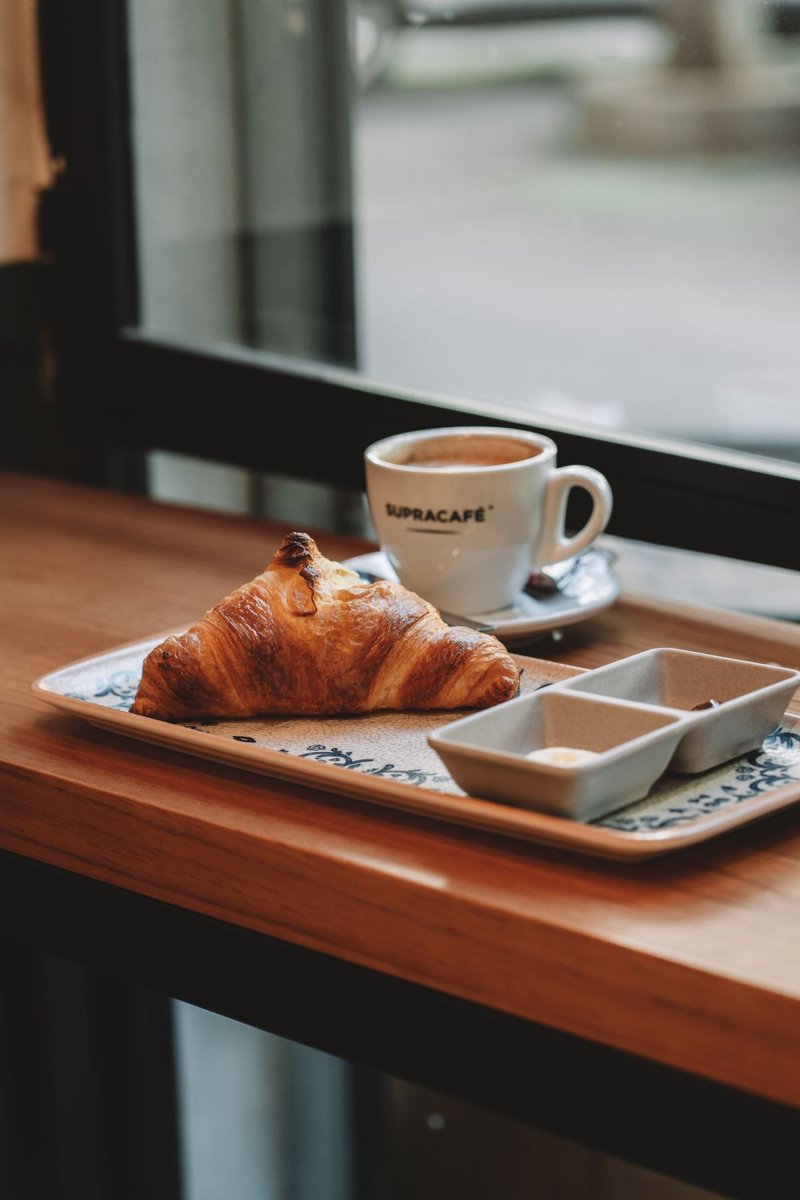 Croissant and coffee on a cafe table beside a window
