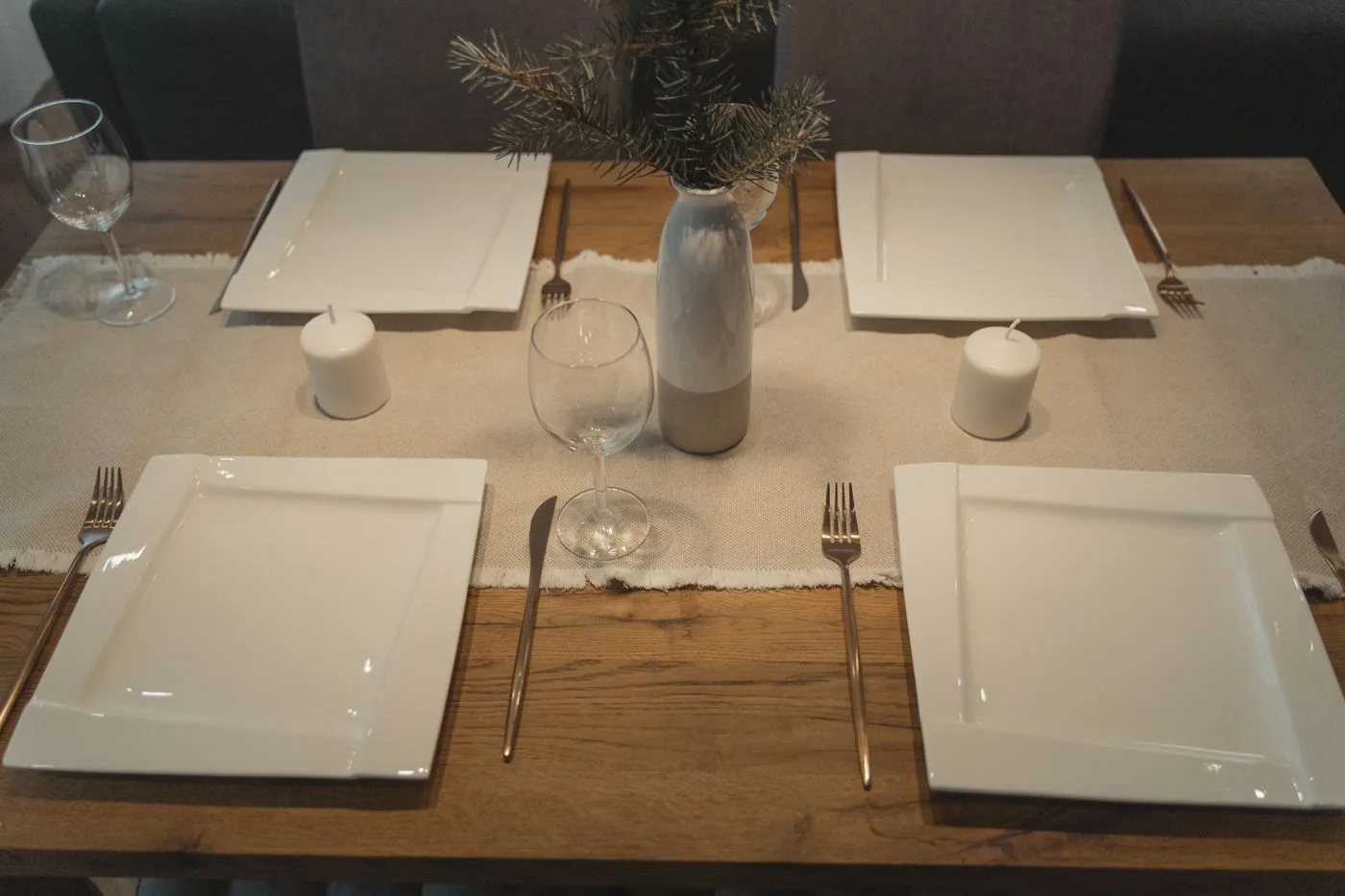 Square white plates, utensils and glasses set on a wooden dining table